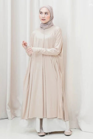 Woman wearing a beige long-sleeve tunic by Mistyvori and hijab against a white curtain background