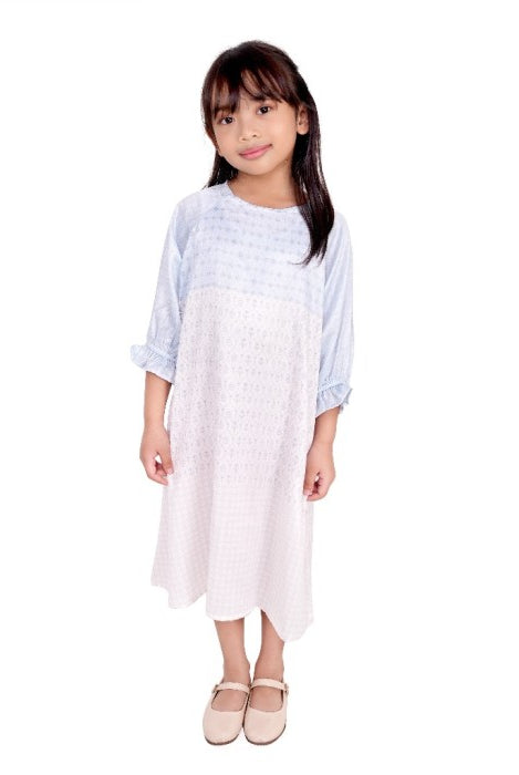 A girl wearing a sky blue tunic with long sleeves and a round neckline.
Seorang anak wanita memakai tunik berwarna biru langit berlengan panjang dan kerah bulat.