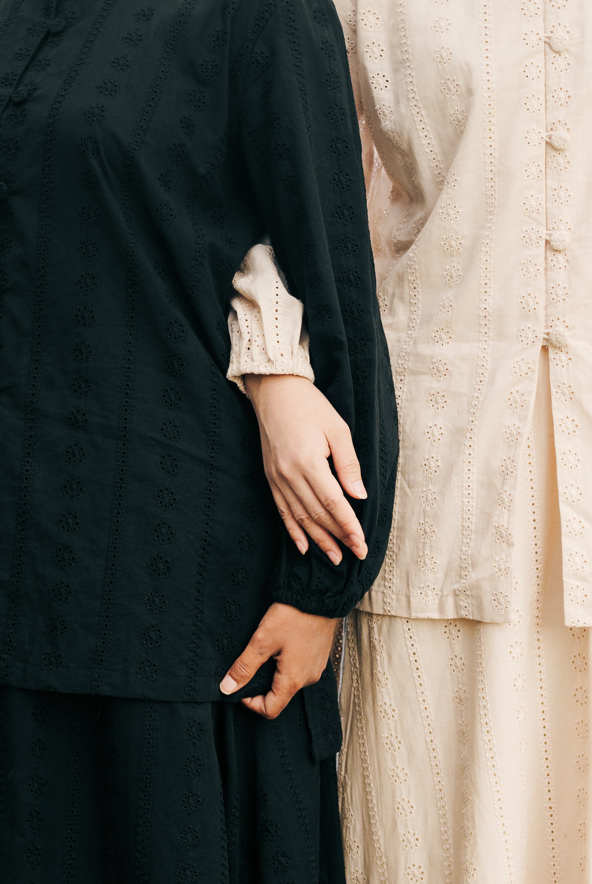 Two people wearing black and light brown long-sleeve tunic with a close-up of their hands.