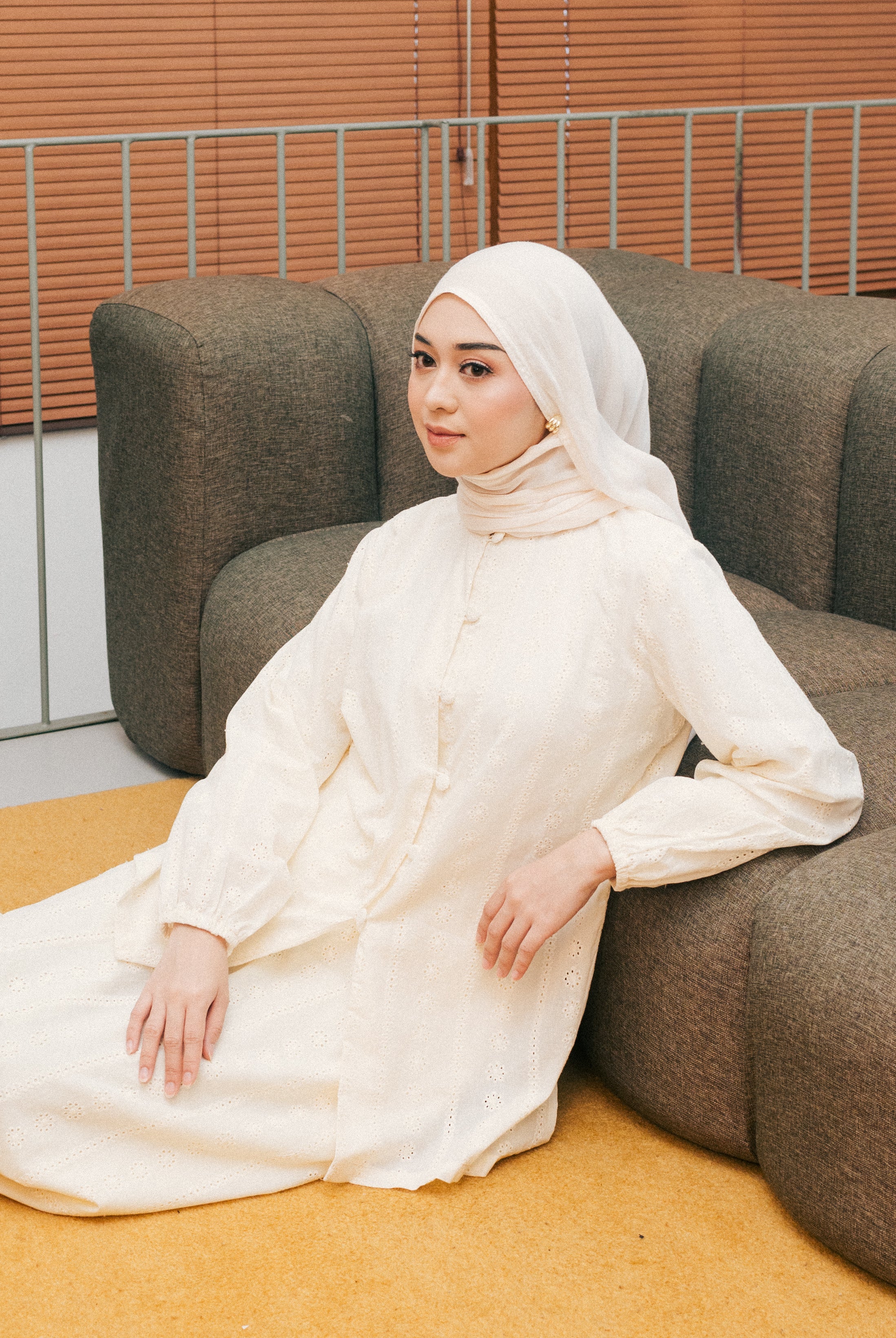 Woman in a broken white tunic from Atala Scarves sitting on a brown couch with a neutral background