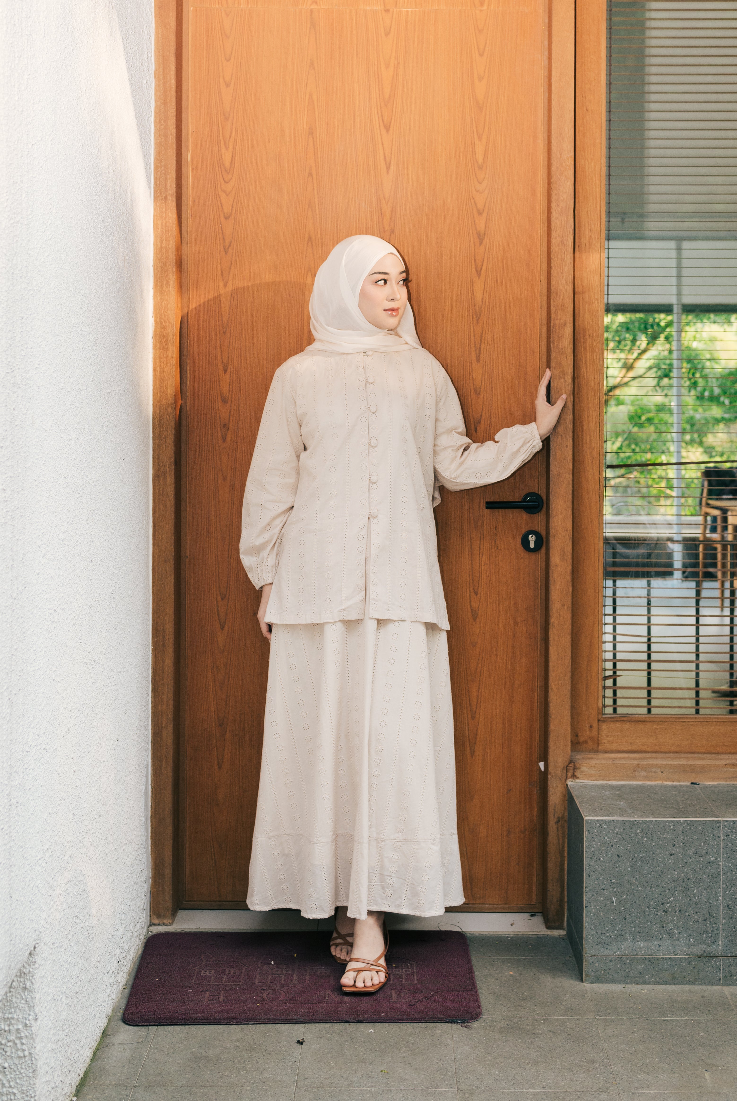 Woman in a light brown tunic from Atala Scarves standing in front of a wooden door.