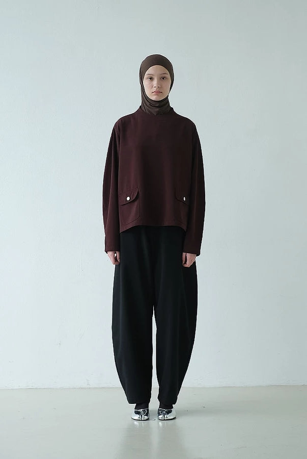 Person wearing a dark brown top with a hijab paired with barrel pants against a white background