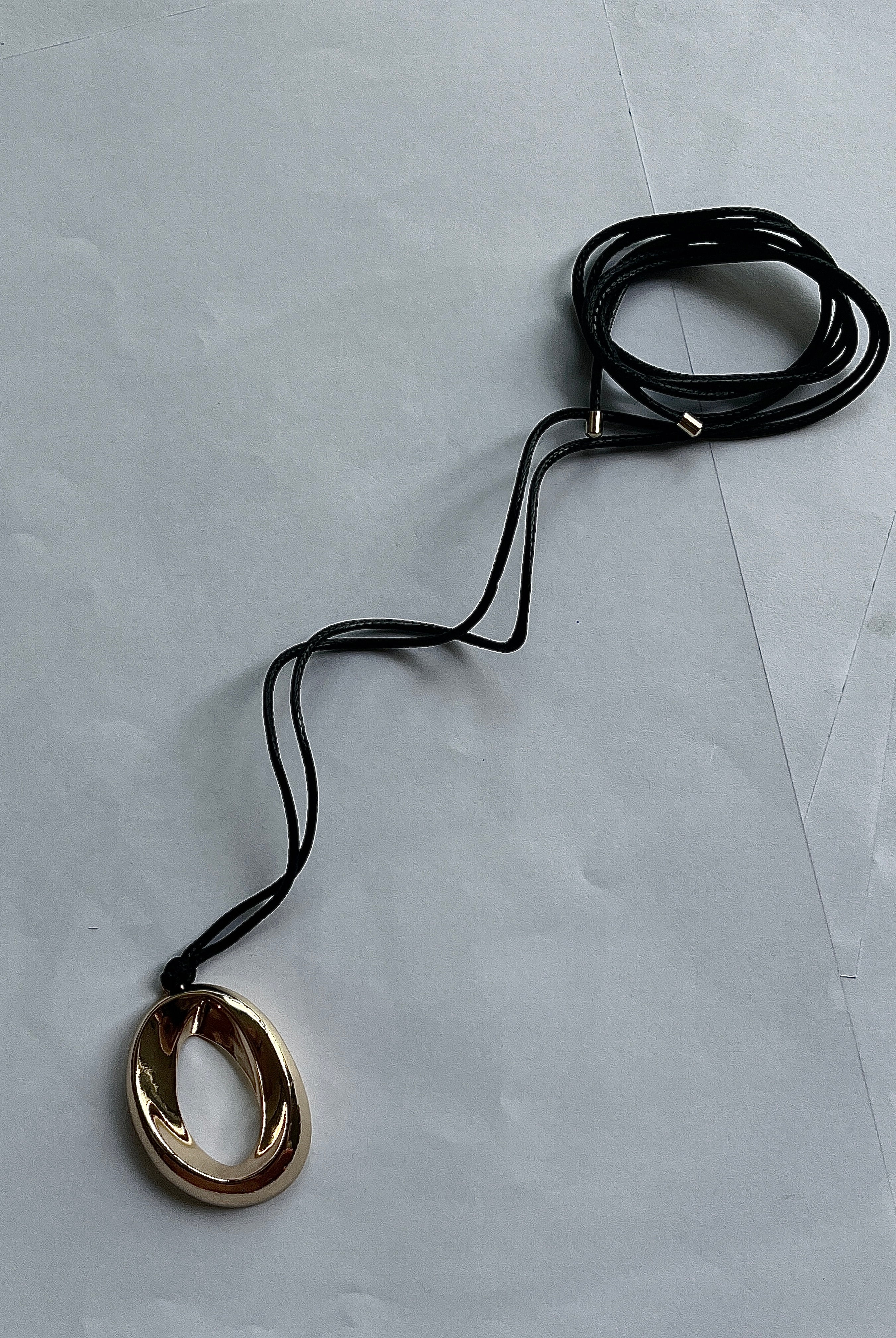 Gold pendant necklace by Darje on a black cord against a light gray background