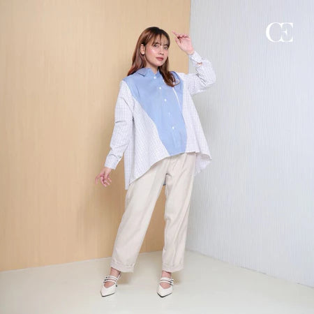 Woman wearing a stripped light blue and checkered white shirt by Casa Elana with beige pants against a neutral background