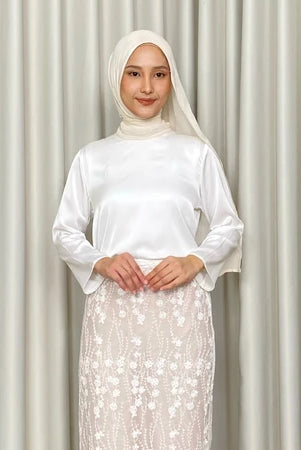 Woman wearing a white top by Kartinis Label with a hijab against a plain background