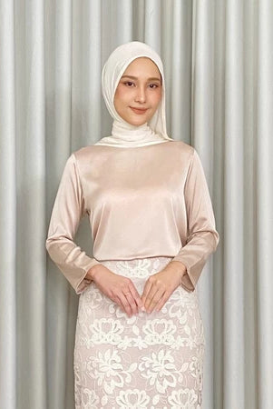 Woman wearing a cream-colored top by Kartinis Label and white lace skirt against a gray curtain background