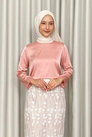 Woman wearing a dusty pink top by Kartinis Label and white hijab with a white skirt against a beige curtain background