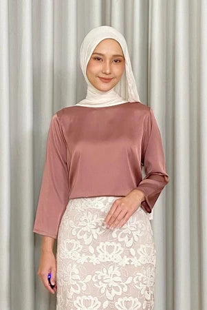 Woman wearing a terracota-colored top by Kartinis Label and white lace skirt against a plain background