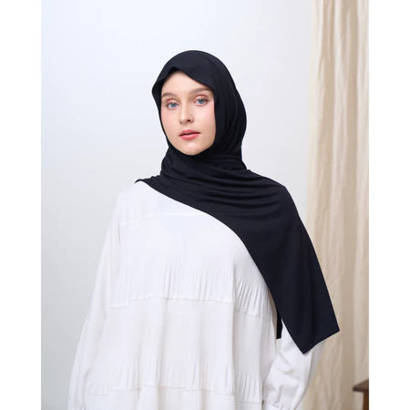Woman wearing a black pashmina hijab and white top against a plain background