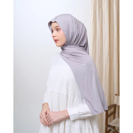 Woman wearing a light gray pashmina hijab and white dress against a plain background
