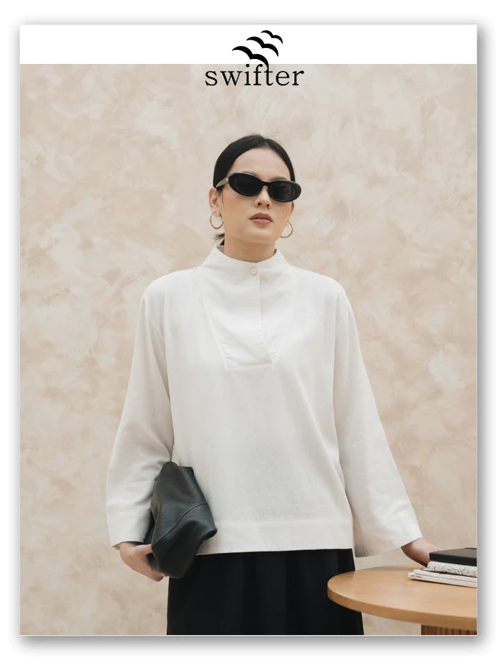 Woman wearing a broken white blouse by Swifter and sunglasses with a beige wall background, featuring the Swifter brand.