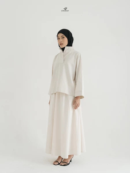 Woman wearing a light brown blouse by Swifter and skirt with a black hijab on a white background