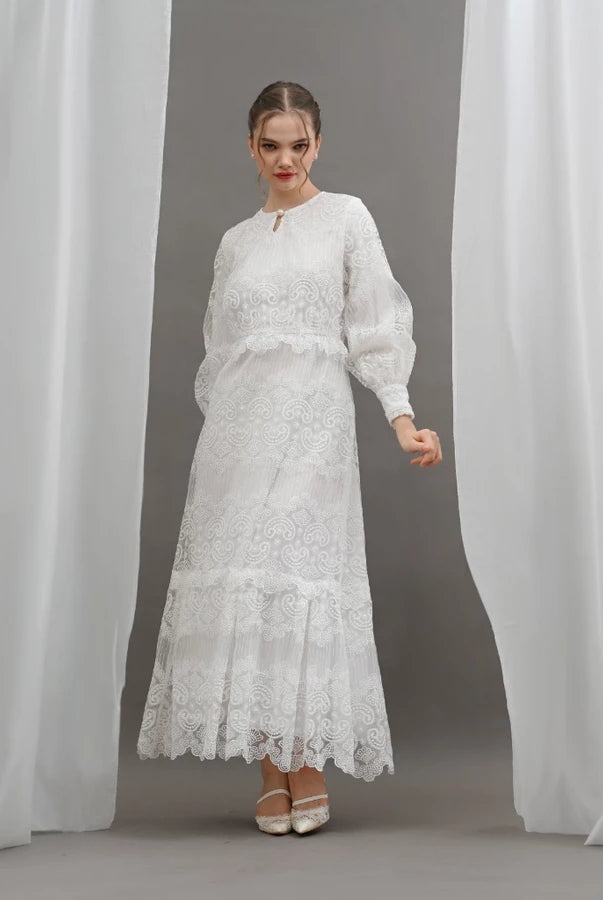Woman wearing a white lace dress by Kasa Heritage standing between two white curtains.