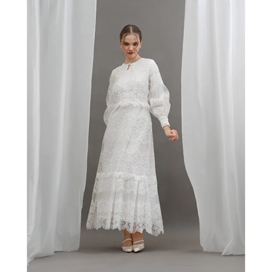 Woman wearing a white lace dress by Kasa Heritage standing between two white curtains.