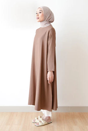 Seorang wanita memakai tunik berlengan panjang berwarna coklat, hijab, dan celana panjang.