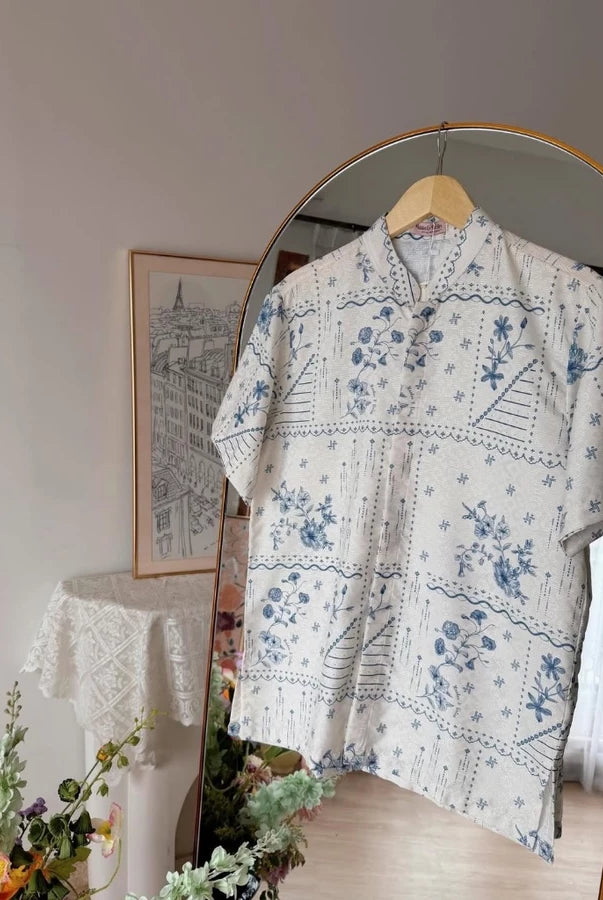 Cream blue floral patterned shirt by Haidee Orlin on a hanger in front of a mirror with decorative elements.