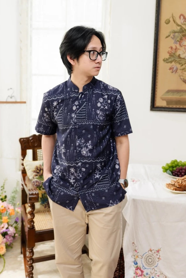 Person wearing a navy patterned shirt by Haidee Orlin in a room with a table and decorative items.