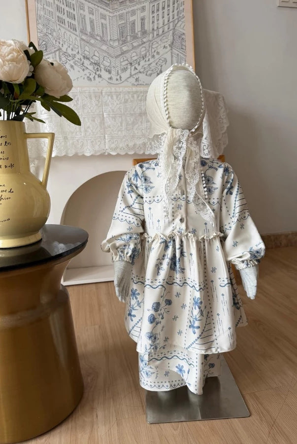 Mannequin wearing a cream blue floral dress by Haidee Orlin in a room with a vase and decorative items.