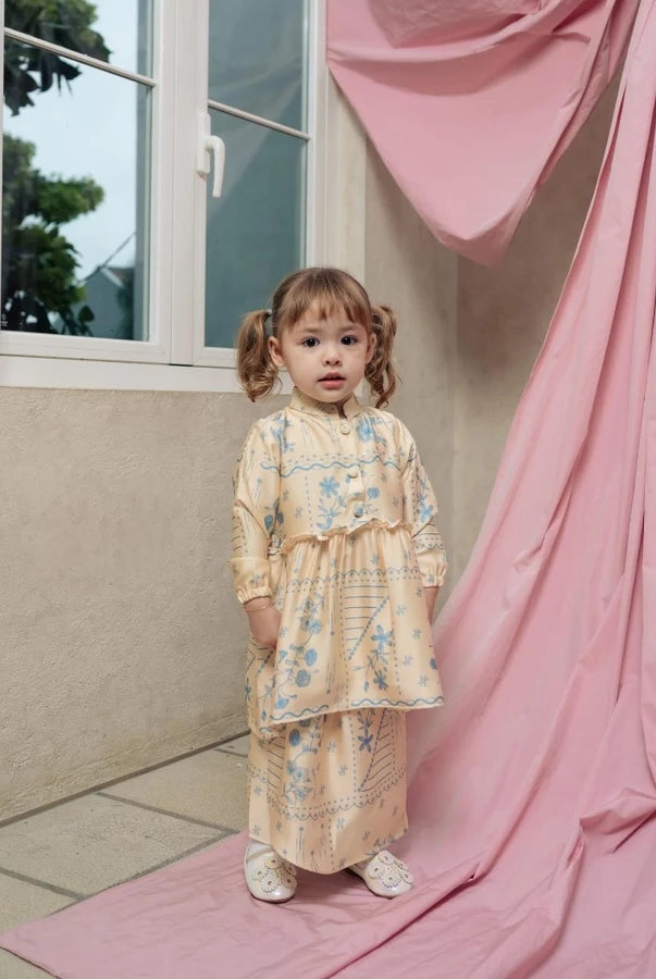 Young girl in a yellow floral dress by Haidee Orlin standing on a pink mat next to a window with pink curtains.