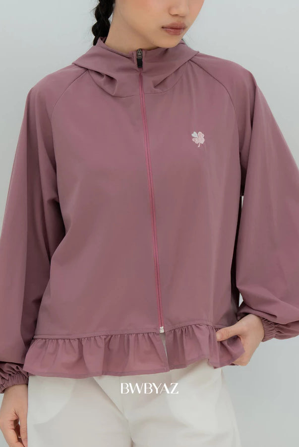 A model wearing a soft mauve lightweight hooded jacket by BWBYAZ with a small embroidered flower on the left chest, paired with white pants. The brand name 'BWBYAZ' is printed at the bottom.