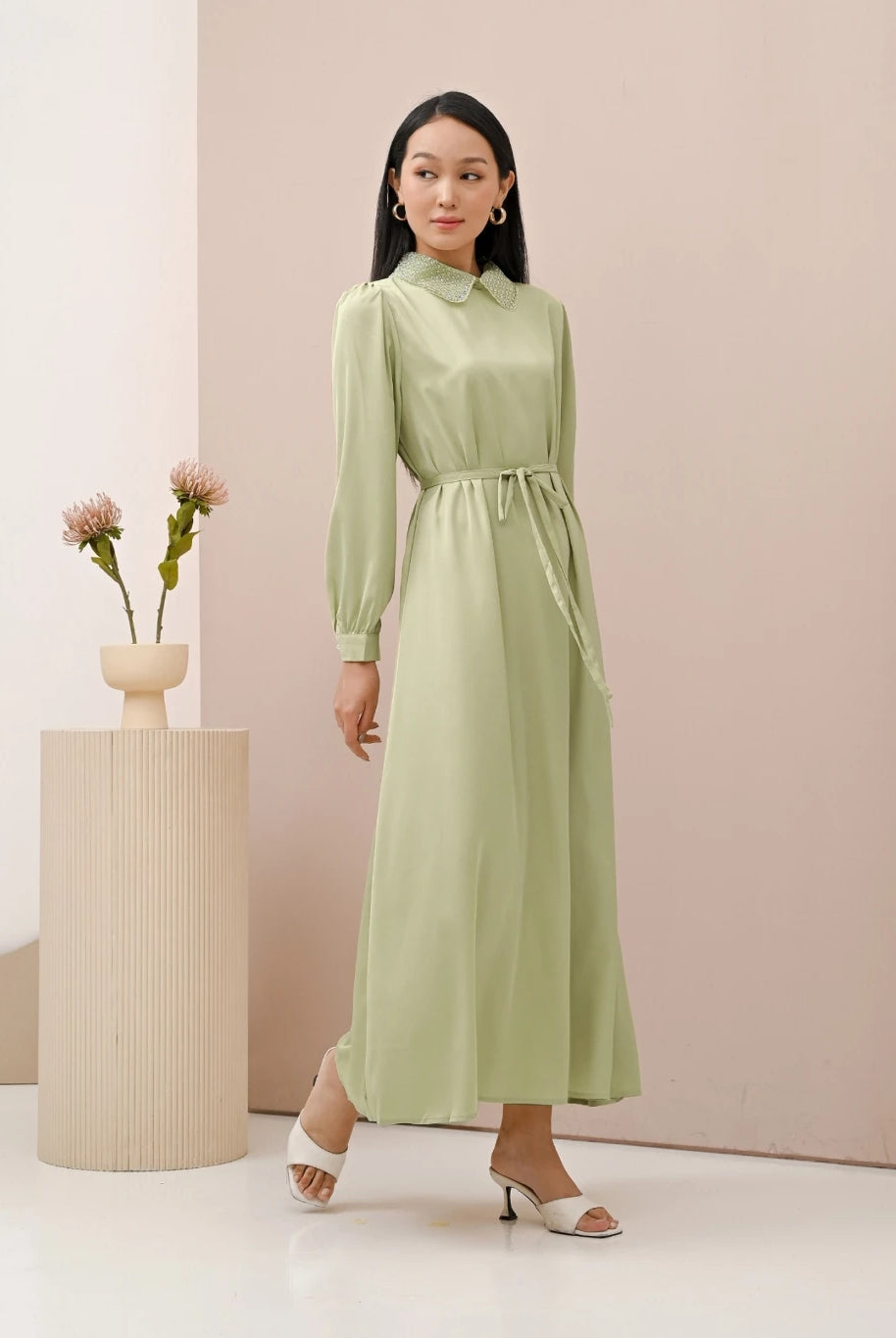 A woman wearing a green dress with long sleeves by Kasa Heritage, featuring a mandarin collar with detail and a detachable belt.
