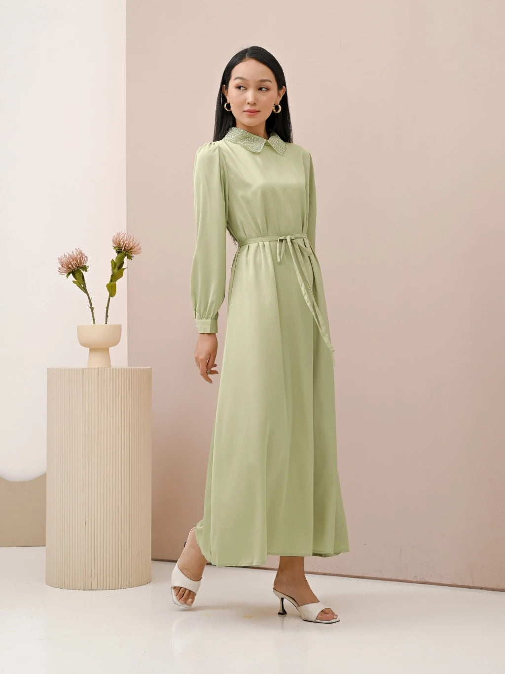 A woman wearing a green dress with long sleeves by Kasa Heritage, featuring a mandarin collar with detail and a detachable belt.