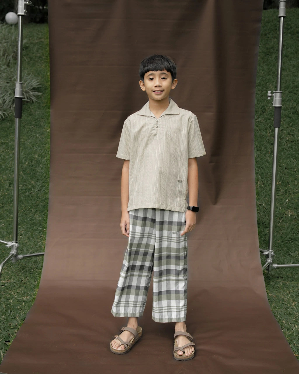 Child standing in front of a brown backdrop wearing grey plaid pants by Mistyvori on a brown background