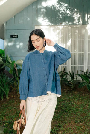 Woman wearing a blue top from Haidee Orlin and white pants outdoors with greenery around