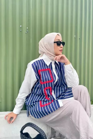 Person wearing a blue and white striped shirt by Abame and sunglasses, standing against a green fence.