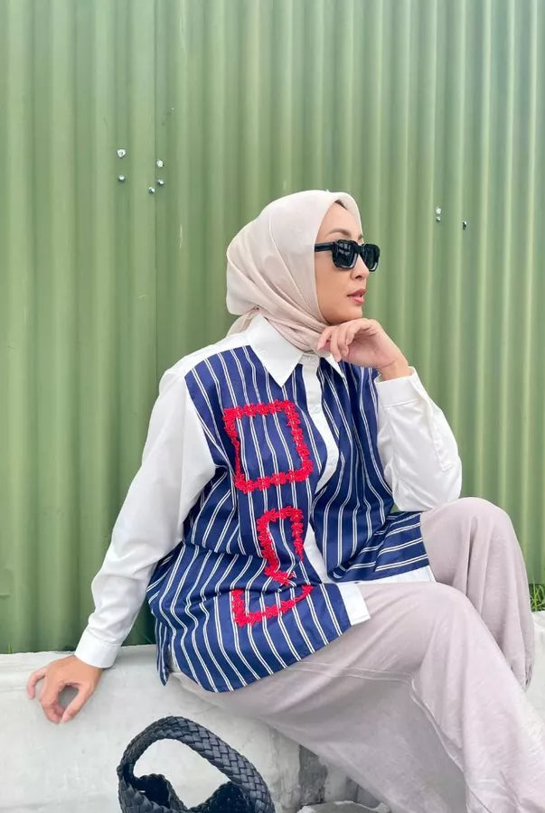 Woman wearing a blue and red striped shirt by Abame against a green corrugated metal background.