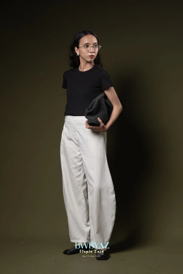 Person wearing a black t-shirt and white barrel pants by BWBYAZ holding a black clutch against a dark background