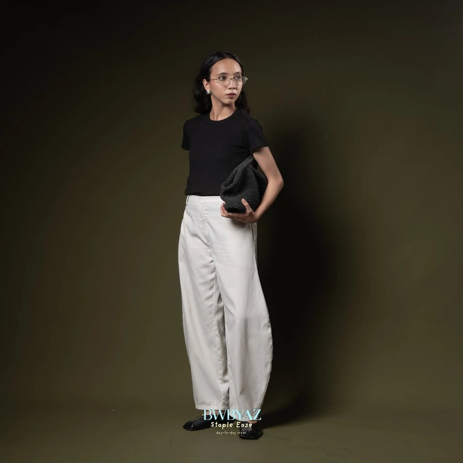 Person wearing a black t-shirt and white barrel pants by BWBYAZ holding a black clutch against a dark background