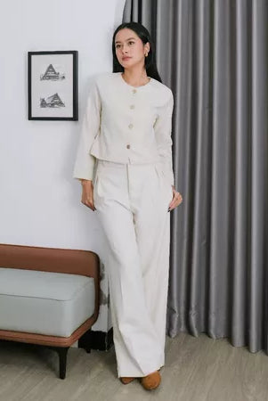 A woman standing in a room wearing a white wide-leg pants by Renaette with a button-up top.