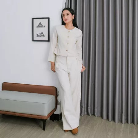 A woman standing in a room wearing a white wide-leg pants by Renaette with a button-up top.