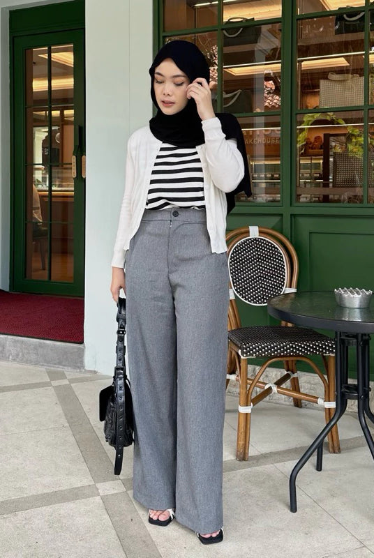 Woman in a striped shirt and gray wide-leg pants by Renaette standing in front of a cafe entrance.