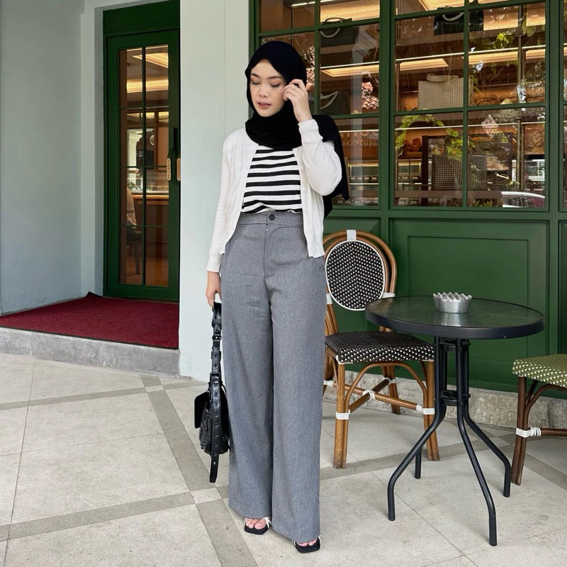 Woman in a striped shirt and gray wide-leg pants by Renaette standing in front of a cafe entrance.