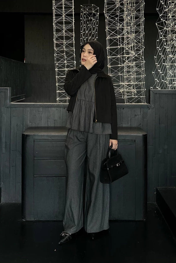 Woman in a black jacket and dark grey pants by Renaette standing in a dark indoor setting with geometric light installations.