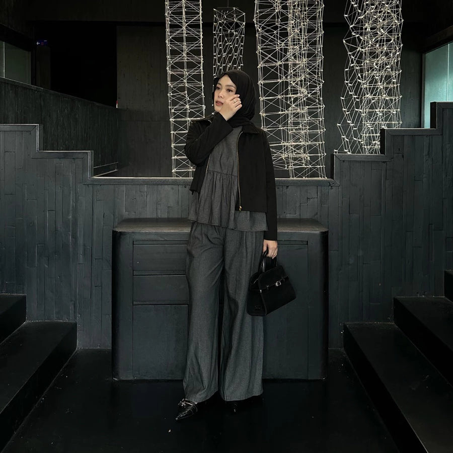 Woman in a black jacket and dark grey pants by Renaette standing in a dark indoor setting with geometric light installations.