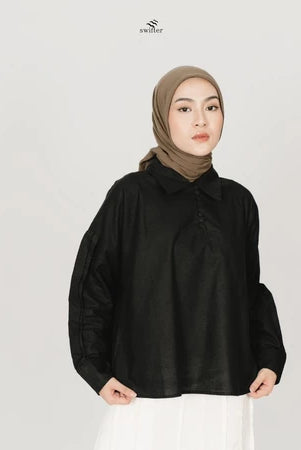 A woman wearing a black polo top with puff sleeves, in front of a white background.