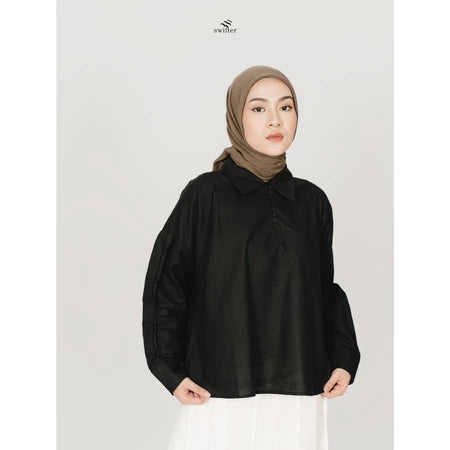 A woman wearing a black polo top with puff sleeves, in front of a white background.