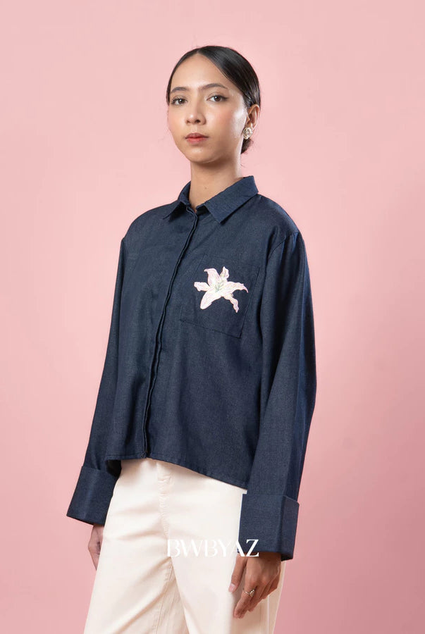 Person wearing a navy blue shirt with a small white floral embroidery by BWBYAZ on a pink background