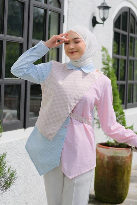 Woman wearing a light blue and pink blouse by Tunique with a hijab, standing outdoors.