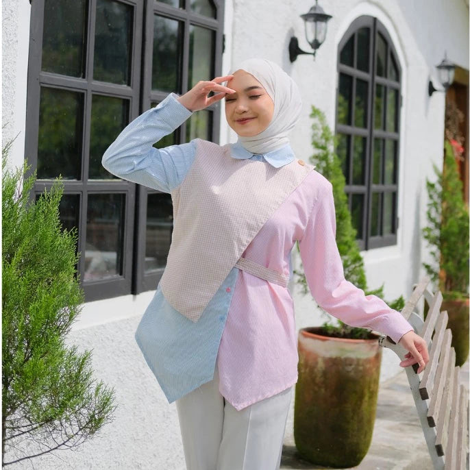Woman wearing a light blue and pink blouse by Tunique with a hijab, standing outdoors.