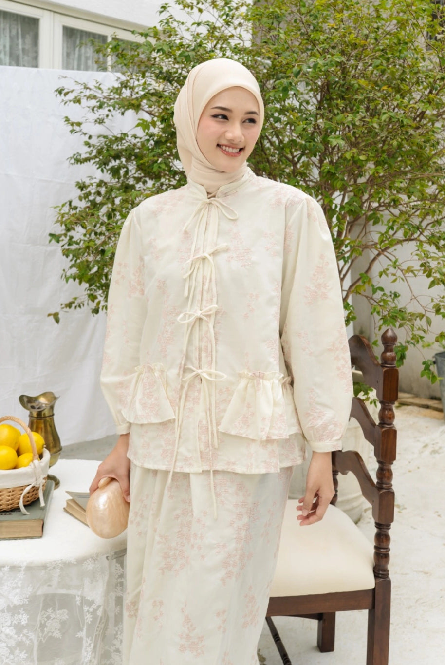 Woman wearing a ivory-colored traditional outfit by Haidee Orlin with a hijab, standing in an outdoor setting.