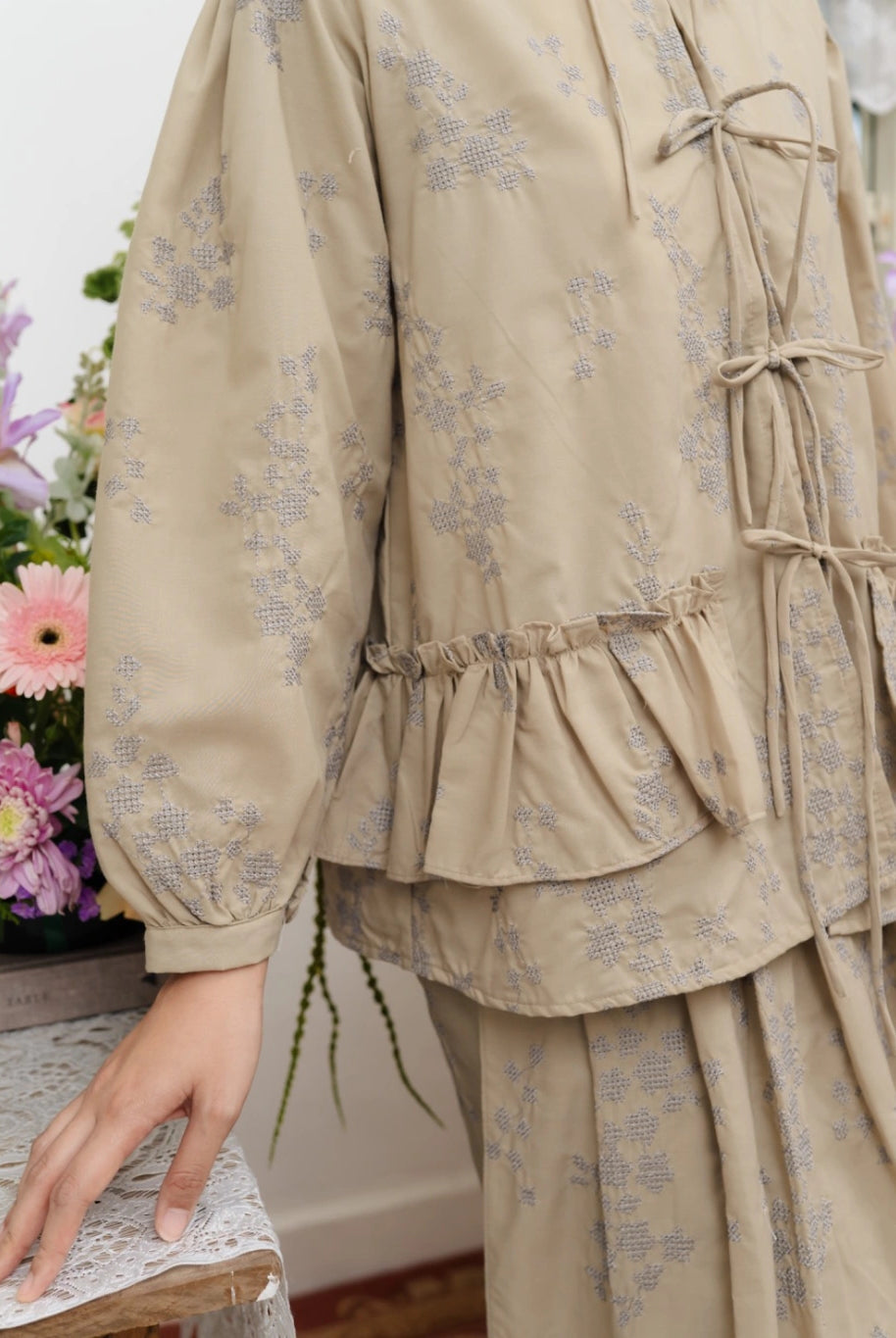 Latte-colored floral-patterned outfit by Haidee Orlin with a blurred background of flowers and books.