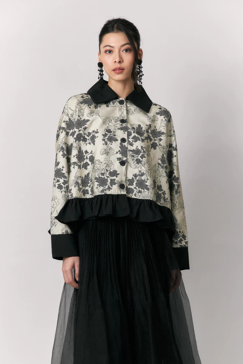 Woman wearing a floral shirt by Studio Tui with black collar and cuffs and a black skirt on a light gray background