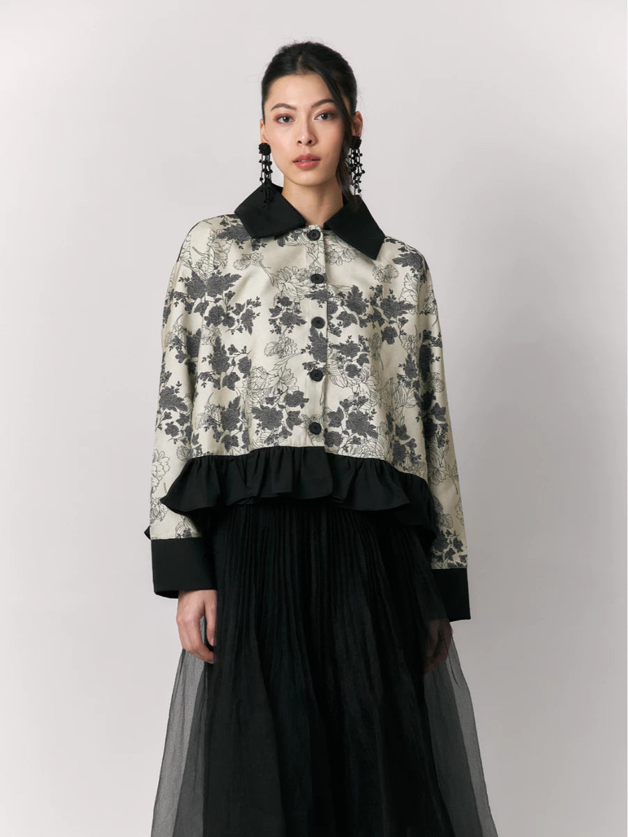 Woman wearing a floral shirt by Studio Tui with black collar and cuffs and a black skirt on a light gray background