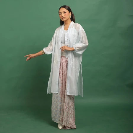 Woman wearing a light blue kebaya by Kartinis Label with a sheer overlay against a green background