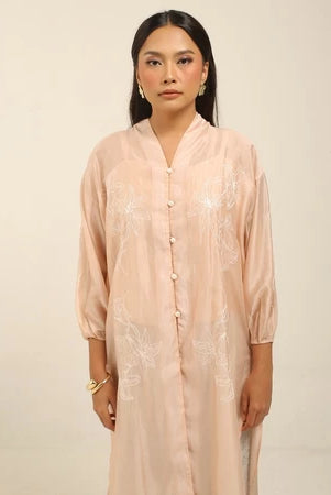 Woman wearing a peach colored embroidered kebaya by Kartinis Label against a beige background