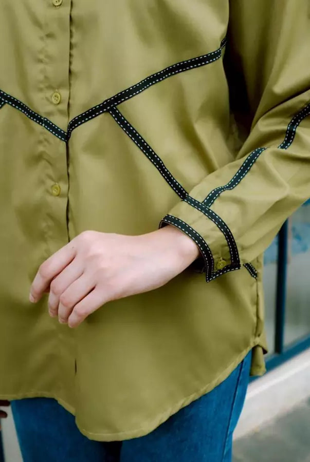 Green shirt by Abame with black trim worn by a person, blurred background